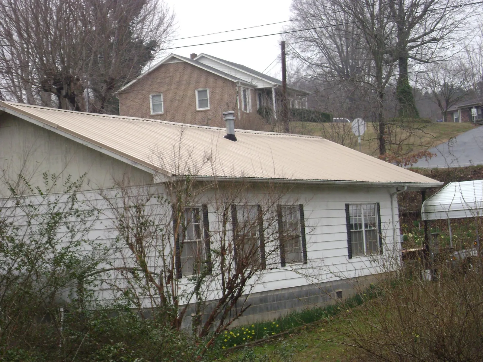 Tan metal roof on a white sided house set into a hillside — Commercial Roofing by Roofing Brothers in Spring Hill